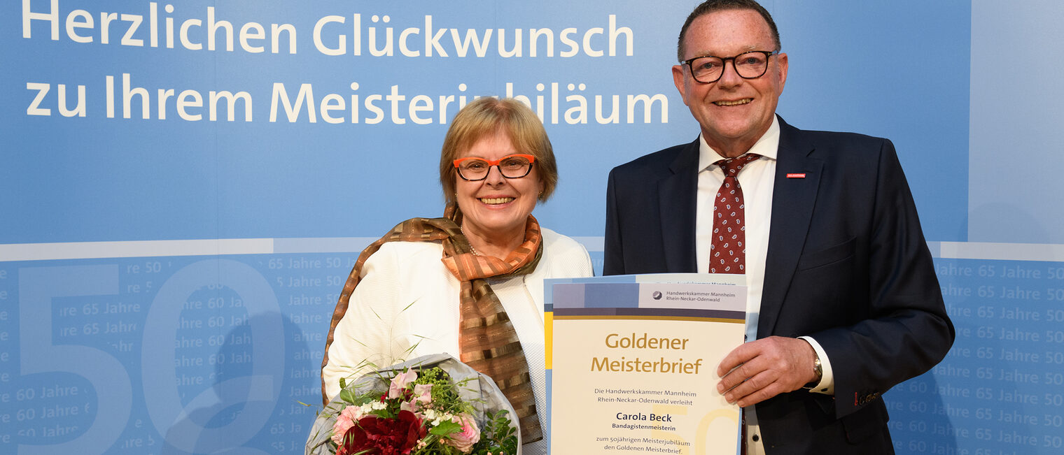 Zwei Personen posieren für ein Foto, in der Mitte wird die Ehrenurkunde gehalten