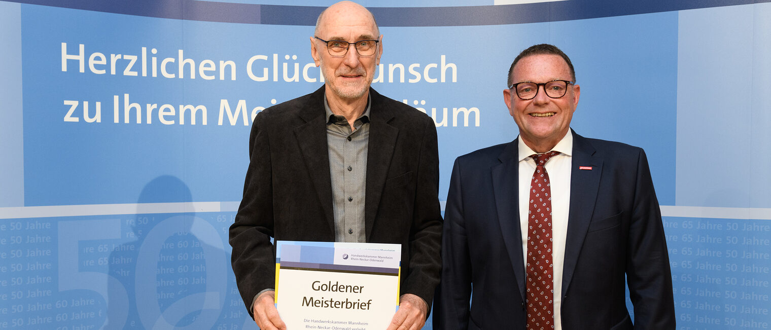 Zwei Personen posieren für ein Foto, davor wird die Ehrenurkunde gehalten