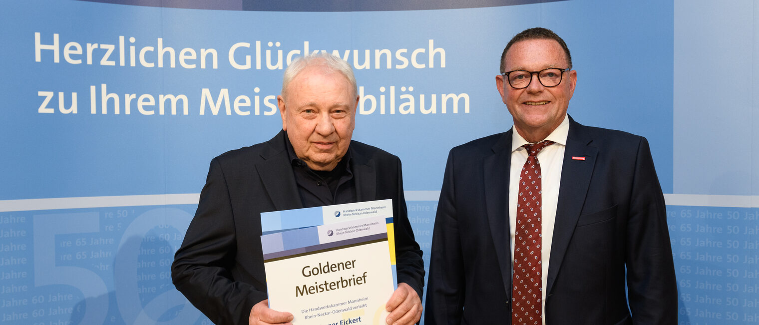 Zwei Personen posieren für ein Foto, in der Mitte wird die Ehrenurkunde gehalten