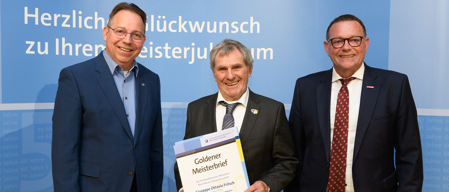 Drei Personen posieren für ein Foto, in der Mitte wird die Ehrenurkunde gehalten