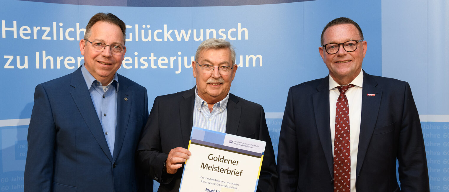 Drei Personen posieren für ein Foto, in der Mitte wird die Ehrenurkunde gehalten