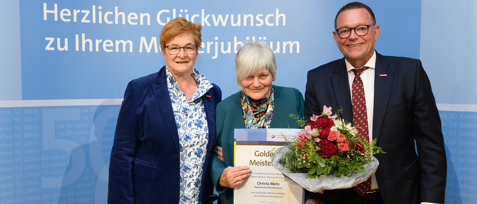 Drei Personen posieren für ein Foto, in der Mitte wird die Ehrenurkunde gehalten