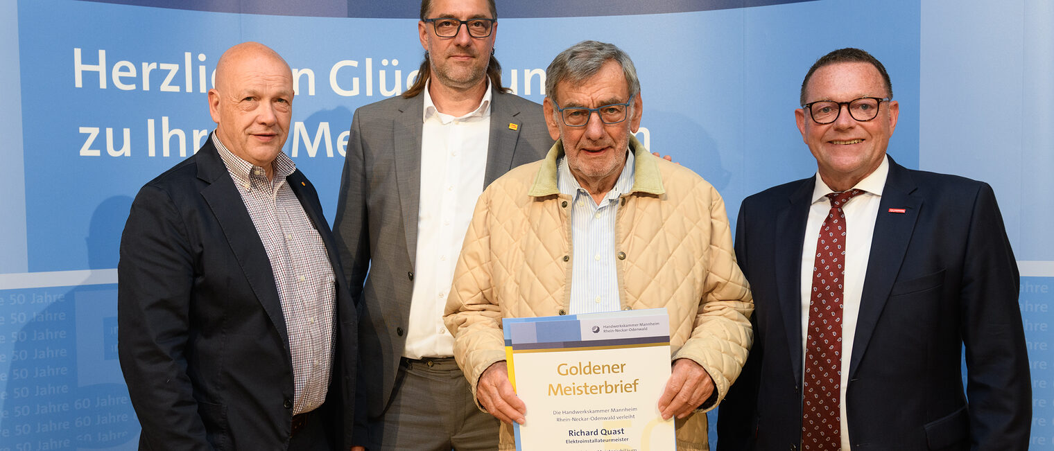 Vier Personen posieren für ein Foto, in der Mitte wird die Ehrenurkunde gehalten