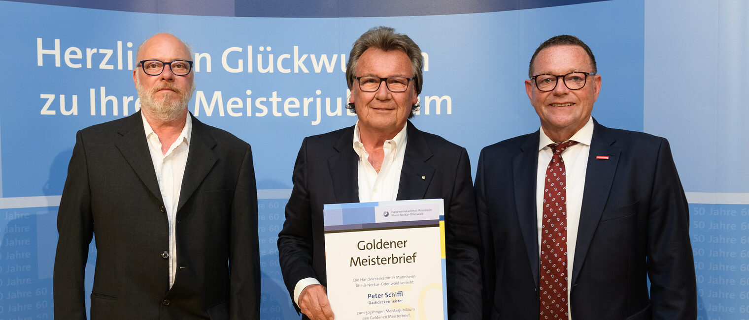 Drei Personen posieren für ein Foto, in der Mitte wird die Ehrenurkunde gehalten