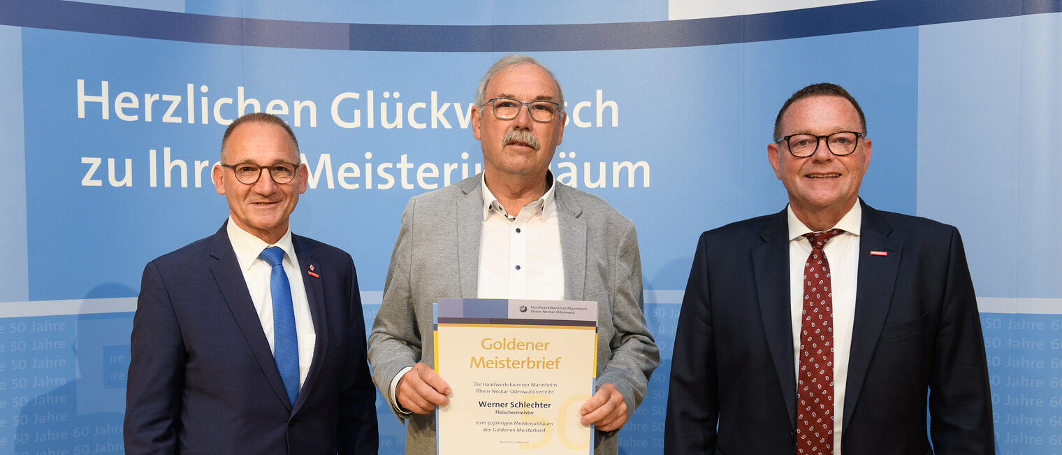 Drei Personen posieren für ein Foto, in der Mitte wird die Ehrenurkunde gehalten