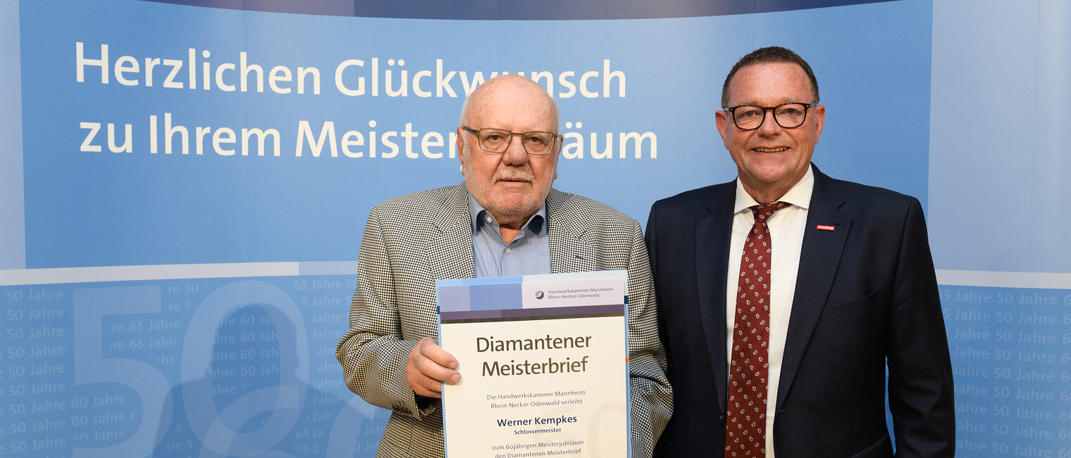 Zwei Personen posieren für ein Foto, in der Mitte wird die Ehrenurkunde gehalten