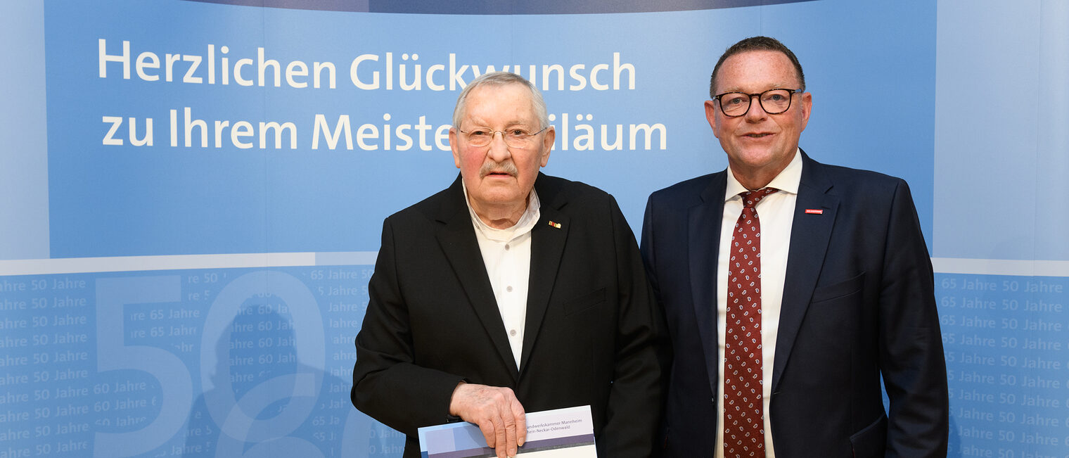 Zwei Personen posieren für ein Foto, in der Mitte wird die Ehrenurkunde gehalten