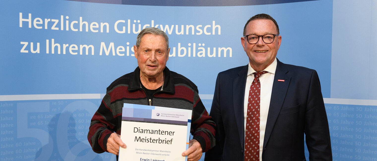 Zwei Personen posieren für ein Foto, in der Mitte wird die Ehrenurkunde gehalten