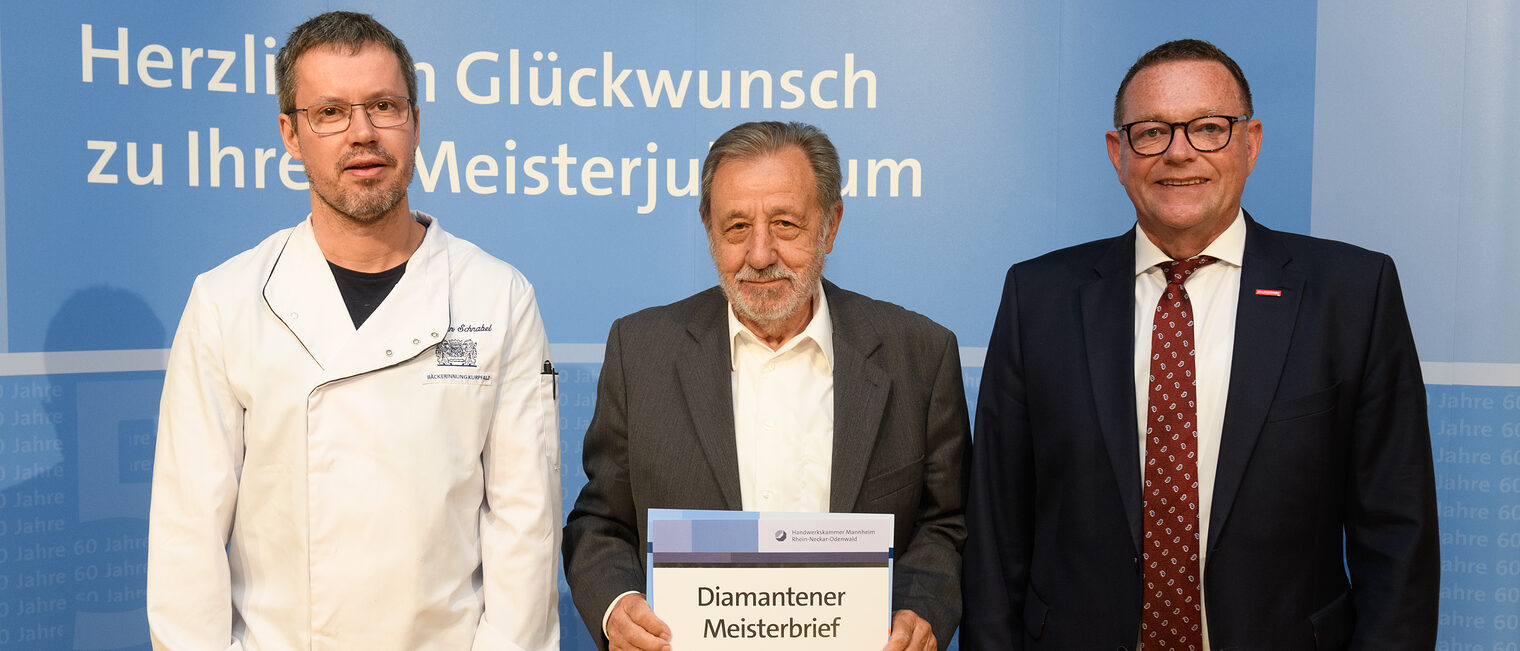 Drei Personen posieren für ein Foto, in der Mitte wird die Ehrenurkunde gehalten