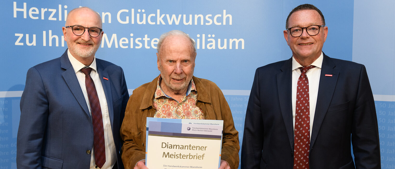 Drei Personen posieren für ein Foto, in der Mitte wird die Ehrenurkunde gehalten