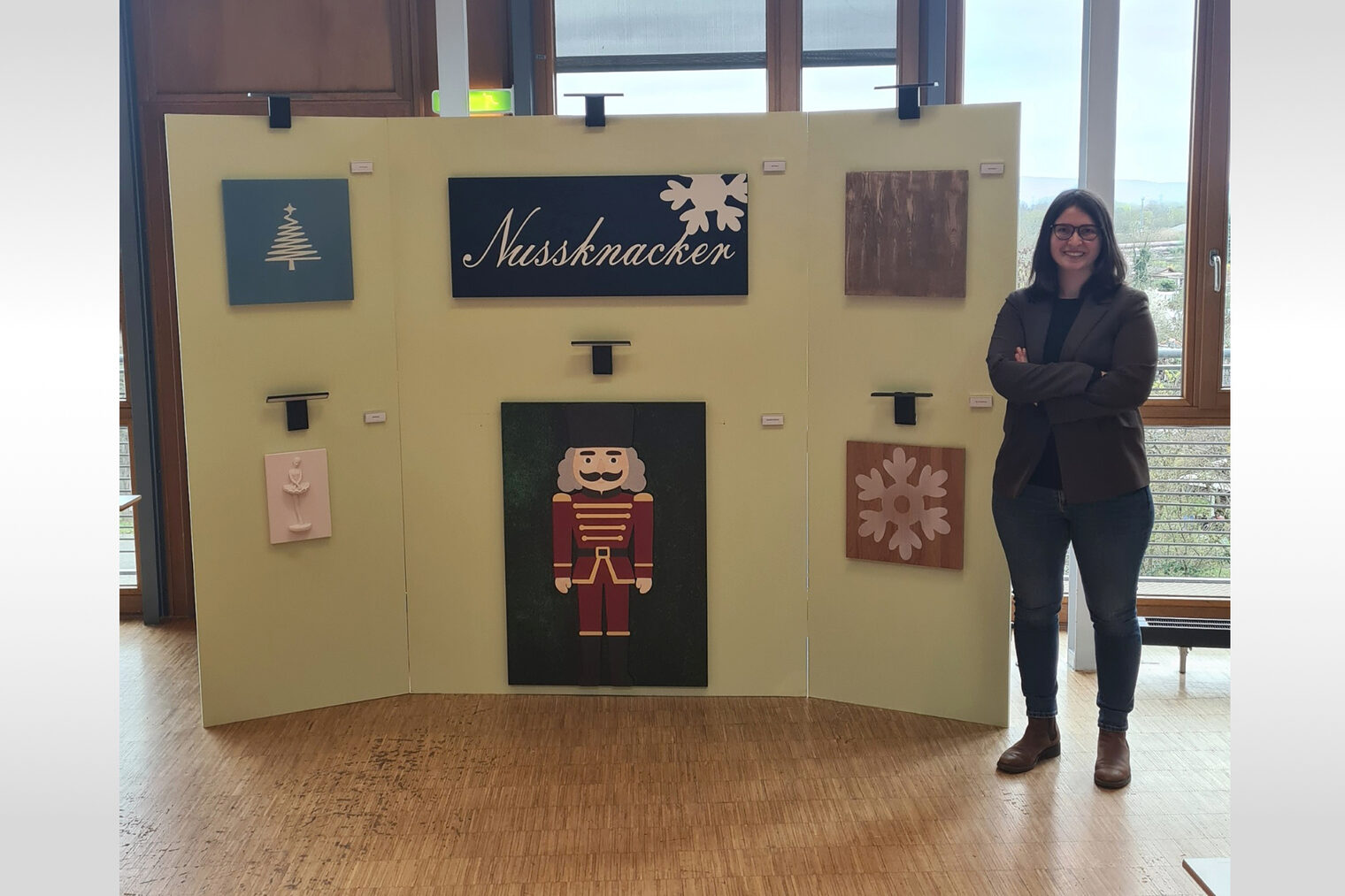 Frau steht neben einer Ausstellung Ihrer Malerarbeit mit Weihnachtsbaum, Nussknacker und weiteren Holzkunstwerken.