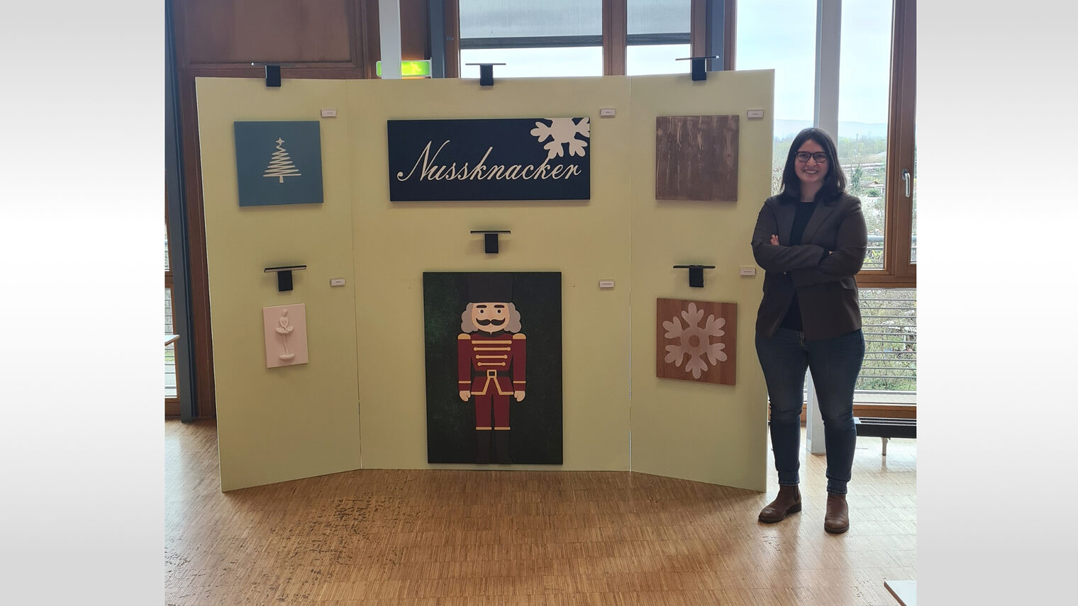 Frau steht neben einer Ausstellung Ihrer Malerarbeit mit Weihnachtsbaum, Nussknacker und weiteren Holzkunstwerken.