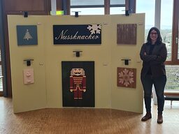 Frau steht neben einer Ausstellung Ihrer Malerarbeit mit Weihnachtsbaum, Nussknacker und weiteren Holzkunstwerken.