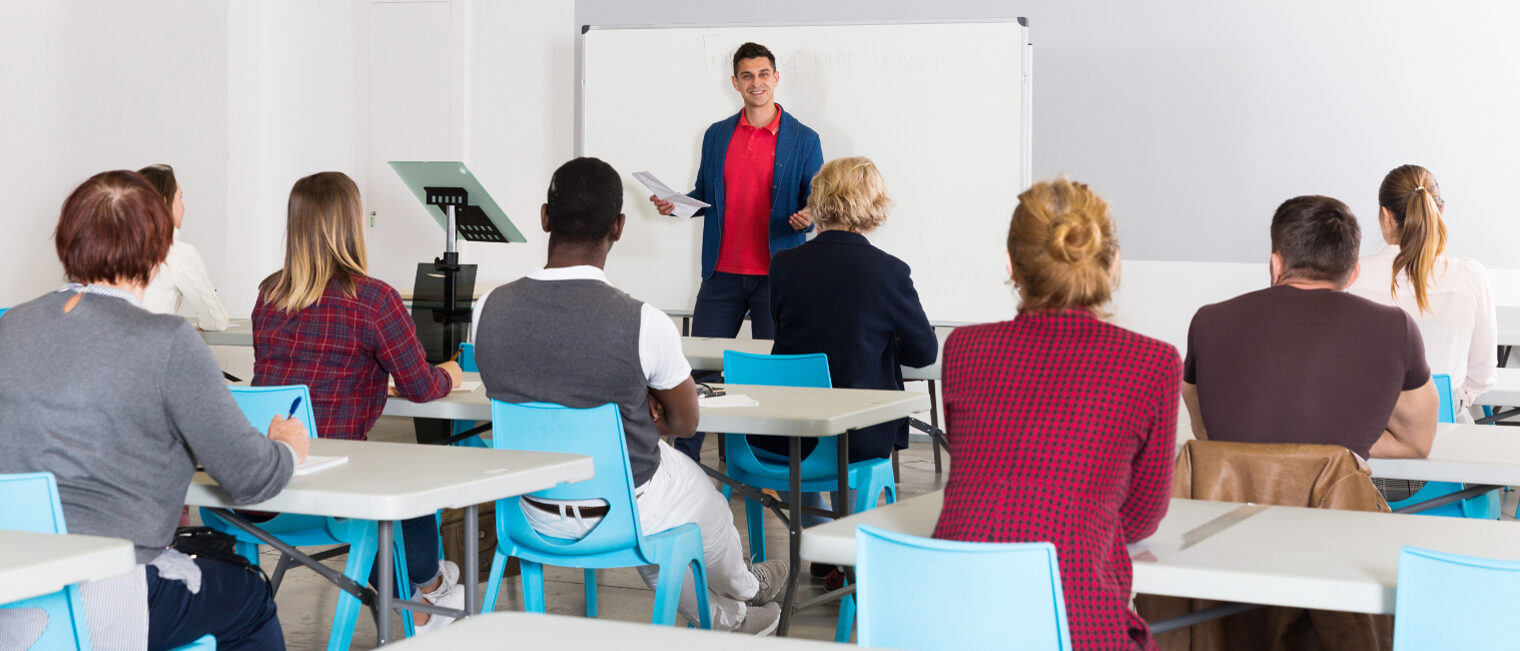 Dozent hält Schulung vor Erwachsenen in einem Seminarraum mit Whiteboard