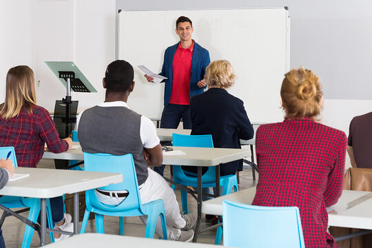 Dozent hält Schulung vor Erwachsenen in einem Seminarraum mit Whiteboard