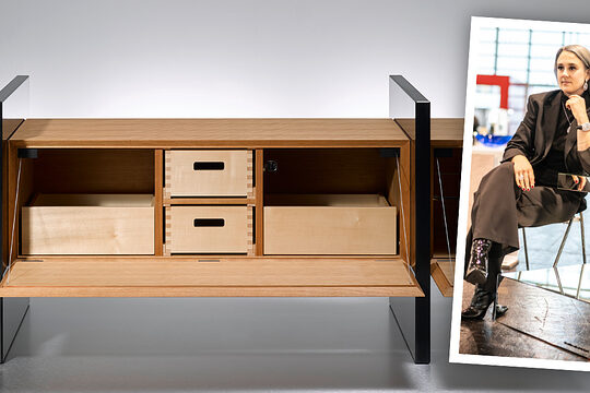 Schreinerin Nicole Doth sitzt neben ihrer Spiegelskulptur; links das geöffnete Holz-Sideboard „3hoch2“ mit schwarzen Seitenwangen.